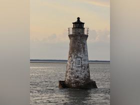 A picturesque lighthouse stands alone in the water, surrounded by calm seas and a pastel sky, creating a serene coastal scene.
