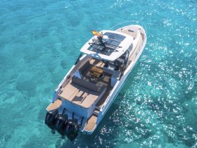 Aerial view of a sleek boat cruising through crystal-clear turquoise waters, showcasing its elegant design and spacious deck — perfect for luxury outings on the water.
