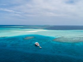 A stunning aerial view of a yacht anchored in crystal-clear turquoise waters, surrounded by a beautiful sandbar — perfect for exploring tropical destinations.