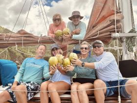A cheerful group enjoys fresh coconuts aboard a sailboat, capturing the essence of a fun sailing adventure in the Caribbean.