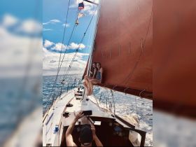 Two friends enjoy a sailing adventure, sitting on the edge of the boat with the ocean in the background — a perfect moment of fun and relaxation on the water.