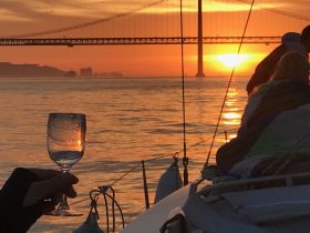 A hand holds a glass of wine against a stunning sunset backdrop while sailing, capturing the essence of a perfect evening on the water.