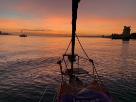 A stunning sunset view from the bow of a boat, showcasing tranquil waters and a distant sailboat, perfect for capturing the essence of evening cruises.