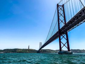 A stunning view of the iconic bridge in Lisbon, framed by the vibrant blue waters and clear sky — a perfect representation of the city's scenic waterfront.