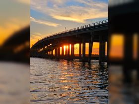A scenic view of a bridge at sunset, reflecting vibrant colors on the water's surface, capturing the beauty of twilight.