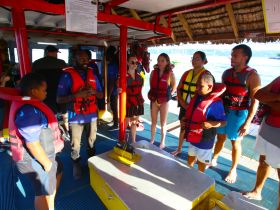 A group of guests participates in a safety briefing aboard a boat, all wearing life jackets, preparing for an exciting water adventure.