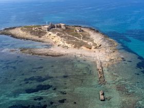 A stunning aerial view of an island with ruins and a rocky coastline, showcasing the crystal-clear waters and inviting scenery — perfect for exploration and adventure.
