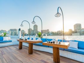 A beautifully designed lounge area on a boat, featuring comfortable seating and a stunning view of the sunset over the city skyline — perfect for dining and relaxation.