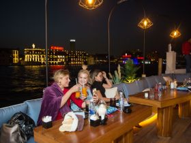 A lively group enjoys cocktails on a beautifully lit boat at night, perfect for celebrations and social gatherings on the water.