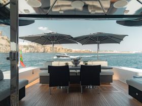 A stylish interior view of a boat's seating area, featuring umbrellas for shade and a scenic backdrop of the coastline — perfect for relaxing on the water.