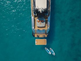 A stunning aerial view of a luxurious yacht anchored in crystal-clear waters, showcasing its elegant design and surrounding paddleboards.