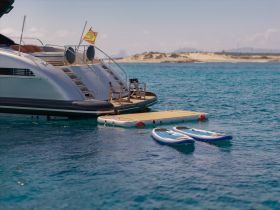 Two paddleboards are ready for use next to a luxurious yacht, showcasing the perfect setup for a day of water activities in a stunning coastal setting.
