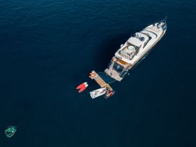 An aerial view of a luxurious yacht with water activities underway, showcasing kayaks and a jet ski, perfect for adventure seekers on the open sea.