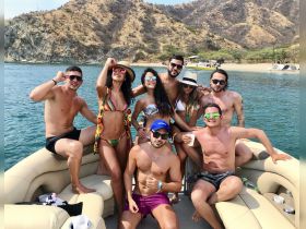 A lively group of friends enjoys a fun day on a pontoon boat, celebrating under the sun with drinks and laughter against a scenic backdrop.