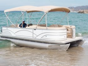 A pontoon boat is seen approaching the shore, with a captain at the helm, showcasing its spacious design perfect for leisurely outings on the water.