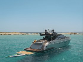 A sleek yacht is anchored in crystal-clear waters, showcasing its elegant design against a picturesque backdrop of a sandy shore.
