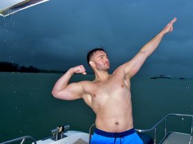 A man strikes a confident pose on the deck of a boat, showcasing a fun moment despite the overcast weather — perfect for adventurous outings on the water.