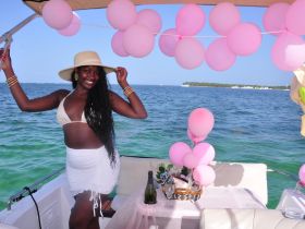 A joyful celebration on a boat with a smiling woman posing amidst pink balloons and a festive setup, perfect for parties or special occasions on the water.