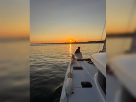 A serene sunset view from a sailing boat, with a person on deck enjoying the tranquil waters — an ideal moment for relaxation and scenic beauty.