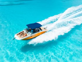 A vibrant speedboat glides through crystal-clear turquoise waters, with guests enjoying the ride — perfect for thrilling adventures on the open sea.