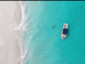 An aerial view captures a boat anchored in stunning turquoise waters, with swimmers enjoying the beach — a perfect scene for summer adventures and water activities.