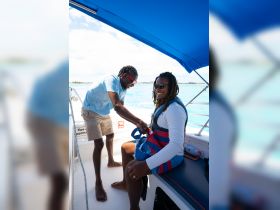 A friendly interaction on a boat as one person assists another in putting on a life jacket, highlighting safety preparations for an exciting water adventure.