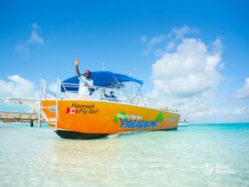 A vibrant parasailing boat named 'Hannah Fly Girl' is seen in clear waters, with the captain waving, showcasing the excitement of water activities in a tropical paradise.