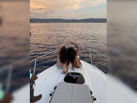 Two girls enjoy a beautiful sunset on a boat, forming a heart shape with their hands — a perfect moment of friendship and celebration on the water.