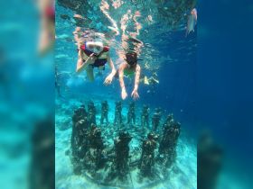 Two snorkelers explore an underwater sculpture park, surrounded by vibrant marine life — a captivating experience for adventure seekers.