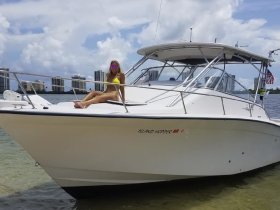 A woman relaxes on the bow of the 'Island Hopper' boat under a sunny sky, showcasing a perfect day on the water.