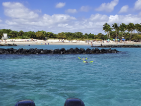A vibrant scene of beachgoers enjoying a sunny day, with snorkelers exploring the clear waters near a rocky jetty — perfect for family outings and water activities.