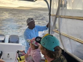 A group enjoys a scenic boat ride at sunset, with a mix of adults and a child actively engaging in the experience — perfect for family outings on the water.