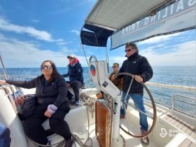 A group of friends enjoys a sailing adventure, with one person at the helm and others relaxing on deck, showcasing the joy of being out on the water.