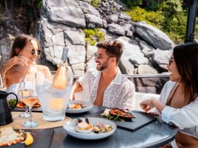 A lively group enjoys a gourmet meal with cocktails on a boat, surrounded by stunning rocky scenery — perfect for memorable dining experiences at sea.