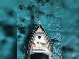 Aerial view of a sleek boat gliding over crystal-clear turquoise waters, showcasing its elegant design and inviting seating area.