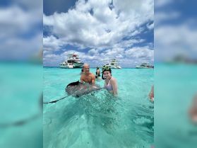 A thrilling encounter as a young girl and a man interact with a stingray in the clear waters, surrounded by boats — a memorable wildlife experience in a tropical paradise.