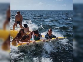 A lively group enjoys a thrilling moment on the water, balancing on a yellow float as waves splash around them — perfect for summer adventures and water fun.