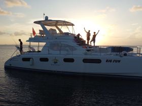 A lively group celebrates aboard the yacht 'BIG FUN' during a stunning sunset, capturing the essence of fun and adventure on the water.