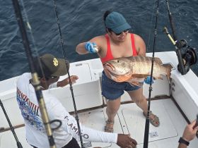 A joyful moment on the water as a woman proudly displays her impressive catch while fishing with friends — a perfect highlight of a day spent at sea.