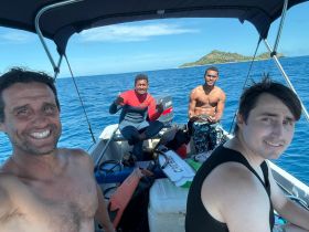 A group of friends enjoys a day out on the water, smiling and posing on their boat with a beautiful island backdrop — perfect for adventure seekers and ocean lovers.