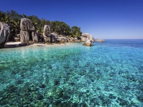 A stunning view of a secluded beach with crystal-clear waters and unique rock formations, perfect for a tropical getaway or eco-tour.