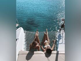 Two friends relax on the netting of a catamaran, enjoying the stunning turquoise waters — a perfect moment for sunbathing and friendship on the water.