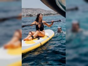 A woman paddleboards while a friend swims nearby, capturing the essence of summer fun on the water — perfect for adventure seekers and beach lovers.
