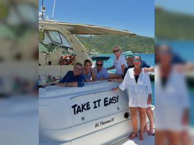 A cheerful group of friends poses on the deck of their boat named 'Take It Easy' in St. Thomas, capturing a moment of fun and camaraderie on the water.