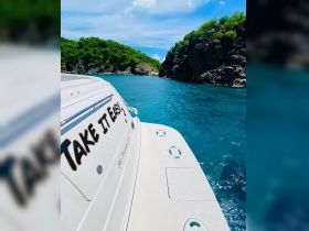 A stunning view of the 'Take It Easy 2' yacht anchored in clear turquoise waters near lush green cliffs, perfect for exploring the beauty of St. Thomas.
