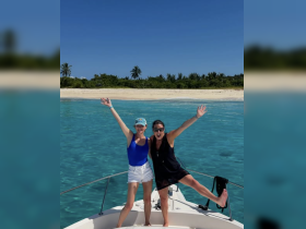 Two friends joyfully pose on the bow of a boat, celebrating their day on the water with a stunning beach backdrop — perfect for memorable adventures and fun in the sun.