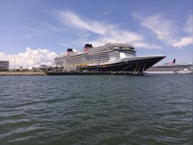 A stunning view of a large cruise ship docked at the harbor, showcasing its impressive structure against a backdrop of blue skies and fluffy clouds.