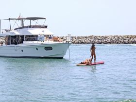 A lively summer scene featuring friends paddleboarding near a yacht, showcasing the perfect blend of relaxation and adventure on the water.