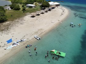 A vibrant scene at a beach with a group enjoying various activities in the shallow waters, including swimming and kayaking — a perfect day for fun in the sun.