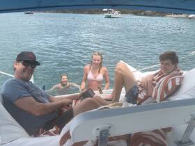 A joyful family enjoys a sunny day on the water, with some swimming and relaxing on the pontoon boat — a perfect setting for summer fun.